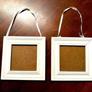 Two small white picture frames with satin ribbons at the top to hang